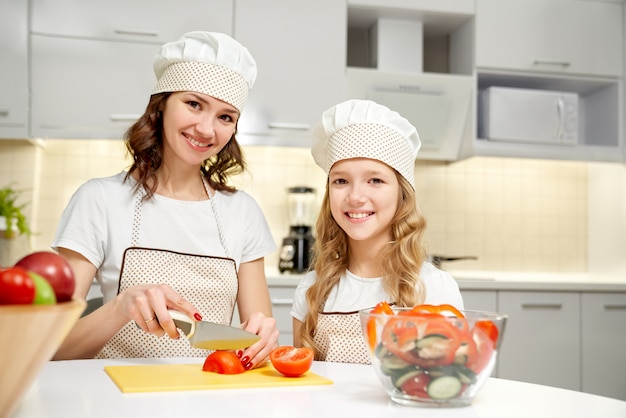 Madre e figlia che posano in cucina, cucinando insalata.