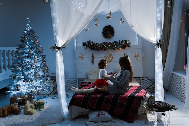 Mother and daughter preparing for christmas celebration. Having fun with family near new year tree. Pregnant woman with daughter.