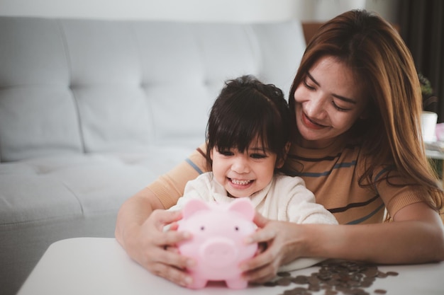 Mother and daughter putting coins into piggy bank. family\
budget and savings concept. junior savings account concept