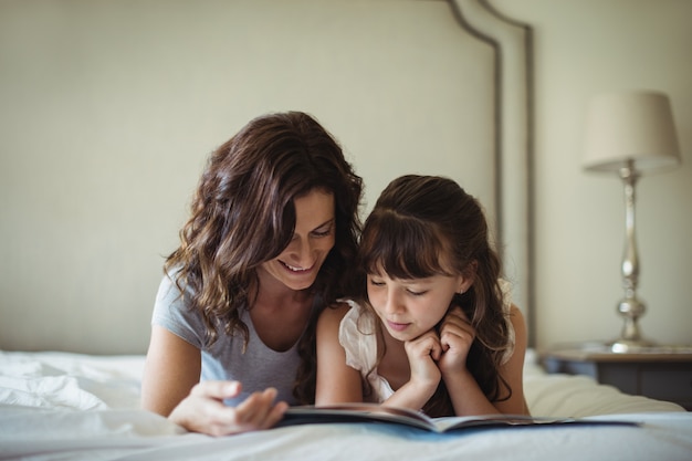 Mother and daughter reading a book while lying on bed