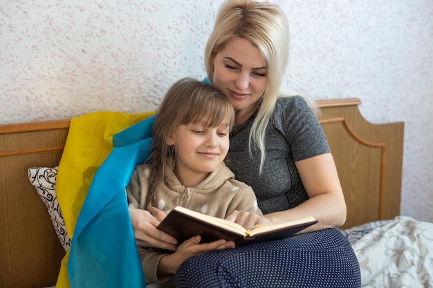 Mother and daughter reading a book with the flag of ukraine in bed