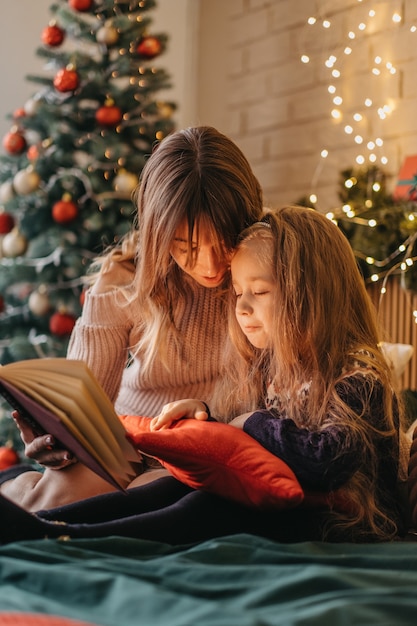 Mother and daughter reading fairytales during Christmas eve, wonderful atmosphere of love and trust, belief in miracles, happy holidays