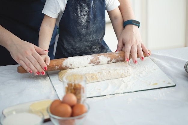 Mother and daughter roll out the dough with a rolling pin