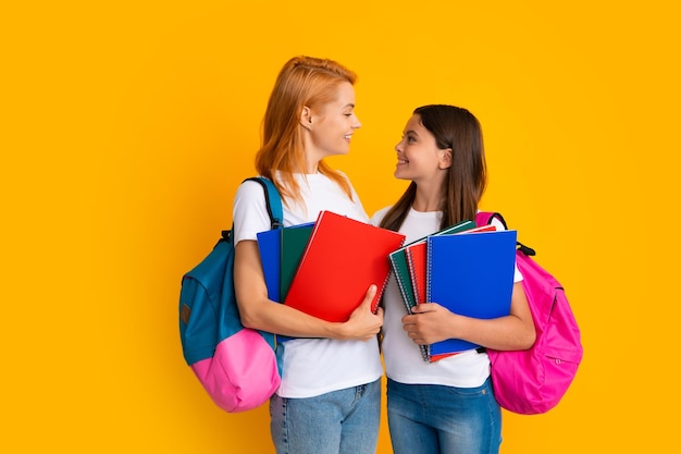 Mother and daughter schoolgirls with school bag ready to learn Back to school Mom and child on isolated yellow studio background Family education