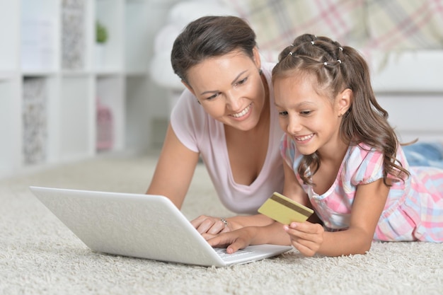 Mother and daughter shopping online while lying on floor