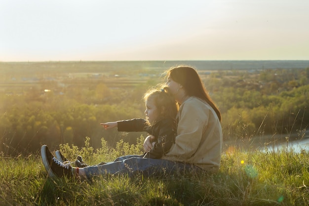 mother and daughter sit on the high bank of the river and enjoy the view of the city