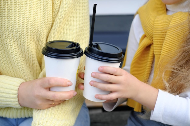 Mother and daughter sit outside and drink hot chocolate closeup shot of paper cups in hands