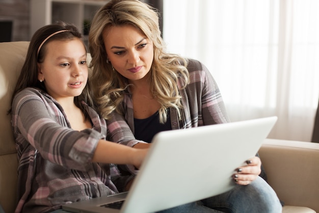 Madre e figlia che si siedono sul divano in soggiorno facendo shopping su internet utilizzando il computer portatile.