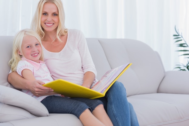 Mother and daughter sitting on couch reading a book