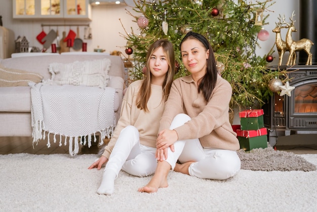Мать и дочь сидят на полу с рождественской елкой на заднем плане