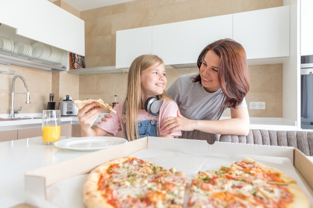 Madre e figlia seduti in cucina, mangiando pizza e divertendosi