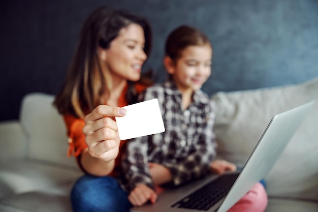 Mother and daughter sitting on the sofa and using laptop for online shopping Mother is holding credit card Selective focus on credit card