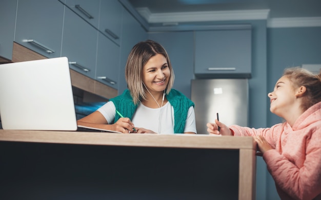 Mother and daughter spending time in the kitchen while the parent is working at the laptop and child is drawing