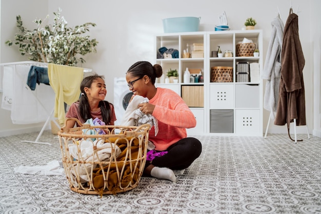 Mother and daughter spending time together in the laundry room while sorting colored clothes prepared for washing in the background bathrobes bathroom wash liquids dryer