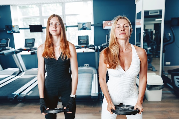 Mother and daughter in sportswear exercising with dumbbells in the gym