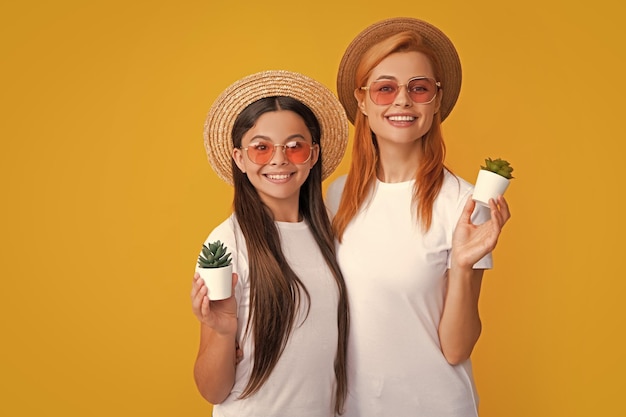 Mother and daughter in straw hat and sunglasses with potted plant on yellow background
