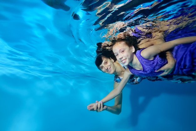 Madre e figlia nuotano insieme sott'acqua in piscina su uno sfondo blu nei raggi di luce