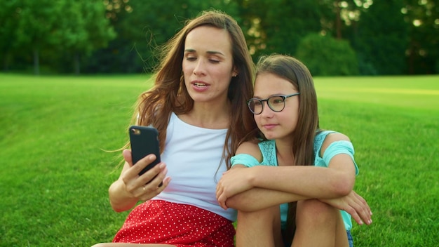 Mother and daughter talking online by video call on cellphone in summer field