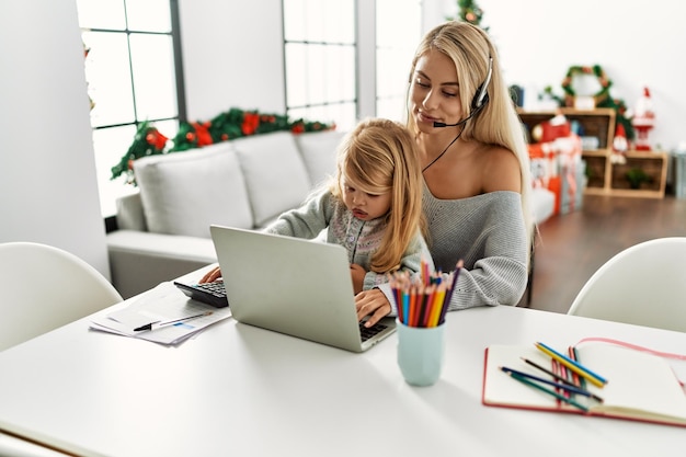 Photo mother and daughter teleworking sitting by christmas tree at home