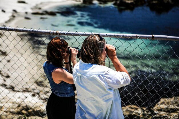 Mother and daughter using binoculars while standing against fence