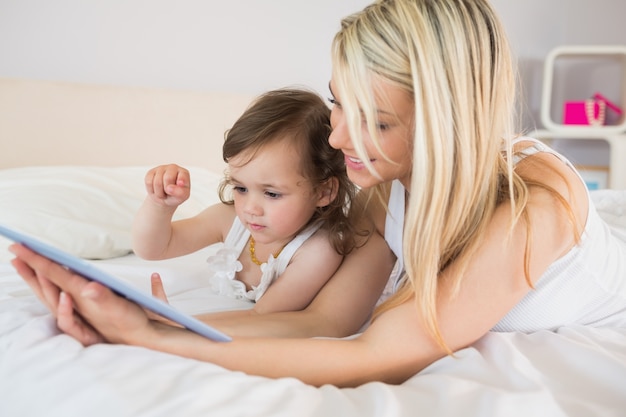 Photo mother and daughter using digital tablet on bed