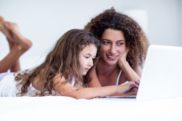 Mother and daughter using laptop on bed