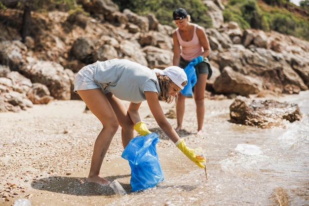 Mother and daughter volunteers cleaning sea beach area from the trash.