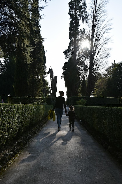 Mother and daughter walking on pathway through beautiful garden Woman and little girl walking across an path into a historic garden Wanderlust Active lifestyle Parenting life path