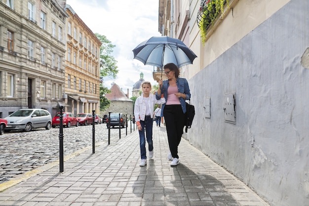 Mother and daughter walking under an umbrella along street