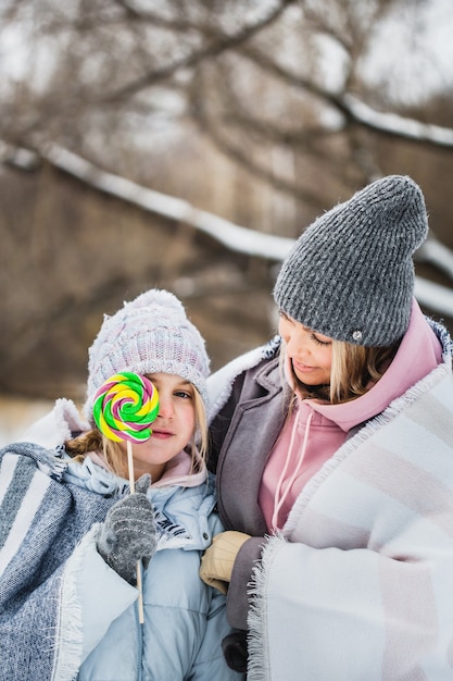 Madre e figlia che camminano nella foresta di inverno, avvolto in una coperta, lecca-lecca, lecca-lecca su un bastone