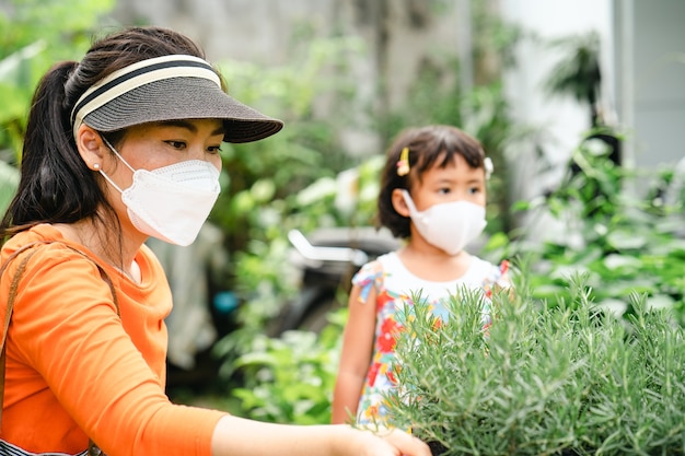 Mother and daughter wearing protective face mask choosing rosemary plant at tree shop