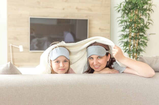 Mother and daughter wearing sleeping mask having fun on couch 