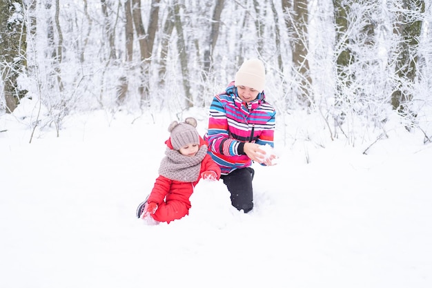 冬の母と娘は自然の中を歩きます。女性と子供の女の子が雪だるまを作る