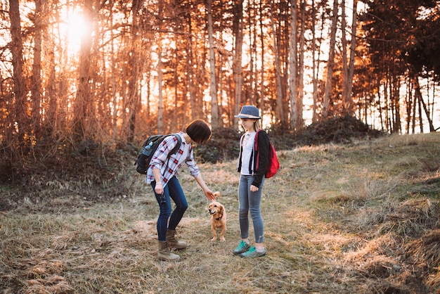 Mother and daughter with dog in forest during sunset