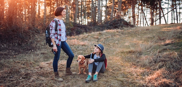 Mother and daughter with dog in forest during sunset