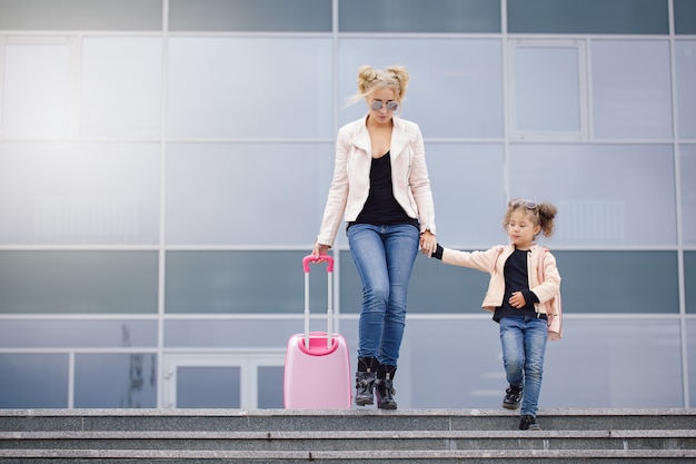 Mother and daughter with pink luggage in pink jacket against the airport