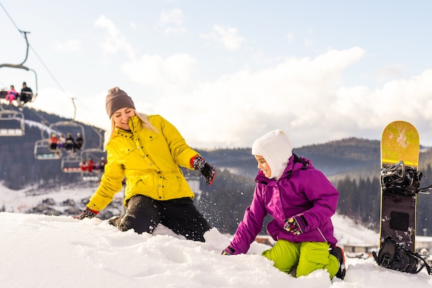 Madre e figlia con lo snowboard stanno giocando nella neve