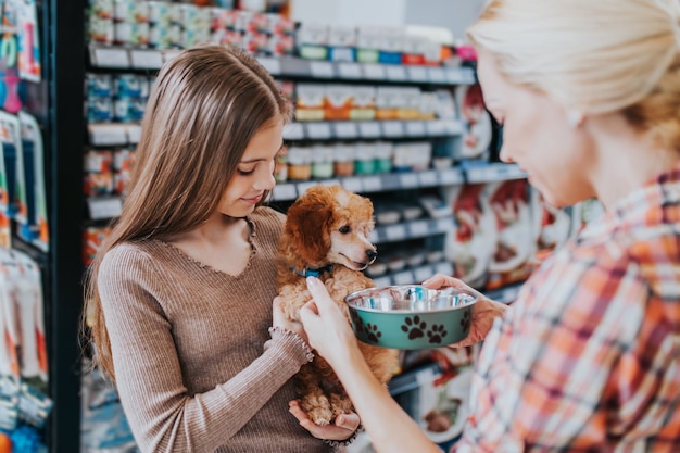 Mother and daughter with their poodle puppy in pet shop.