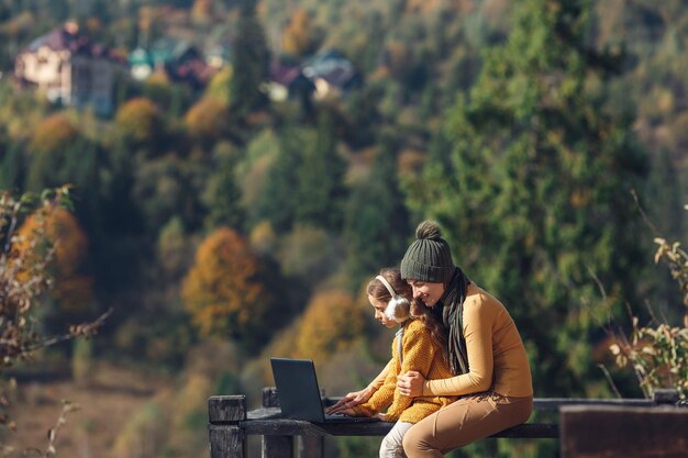 엄마와 딸은 가을에 야외 테라스에서 노트북 작업을 합니다.