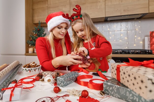 Mother and daughter wrapping christmas gift boxes on the background of decorated kitchen