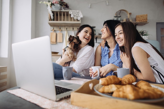 Photo mother and daughters talking and eating croissants in the kitchen