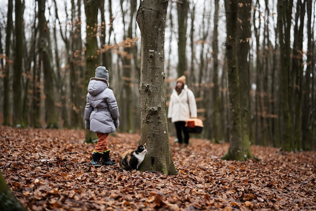 고양이와 함께 걷는 어머니와 딸은 나무에서 야외 플라스틱 케이지 마차를 여행합니다.
