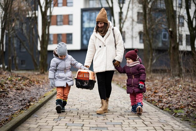 Mother and daughters walking with kitten in travel plastic cage carriage outdoor at park