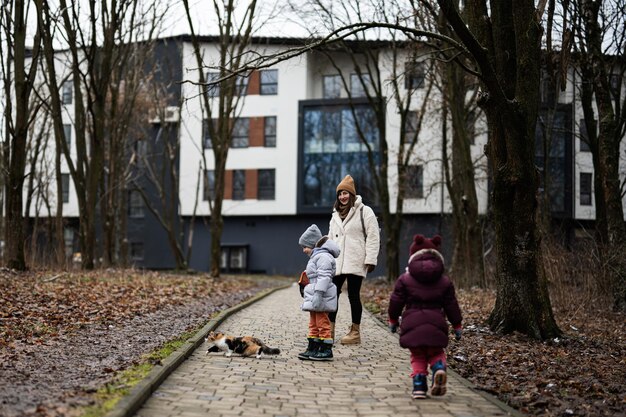 Mother and daughters walking with kitten in travel plastic cage carriage outdoor at park