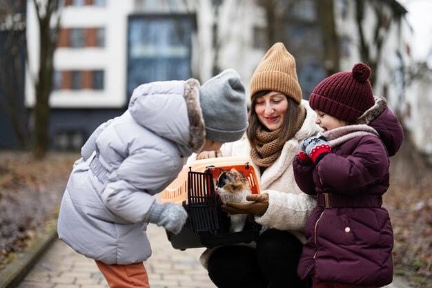 Mother and daughters with cat in travel plastic cage carriage outdoor at park