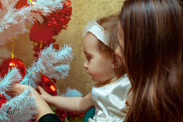 Mother decorates the Christmas tree with her little baby girl