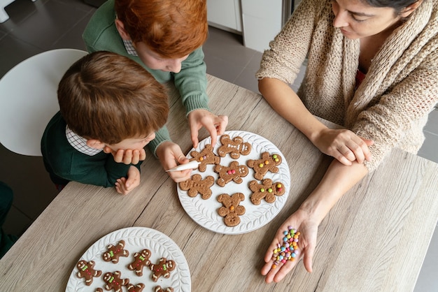 Photo mother decorating gingerbread cookies with children at home