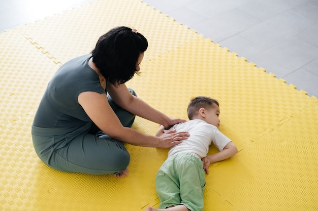 Mother doing physical exercises playing with disabled boy