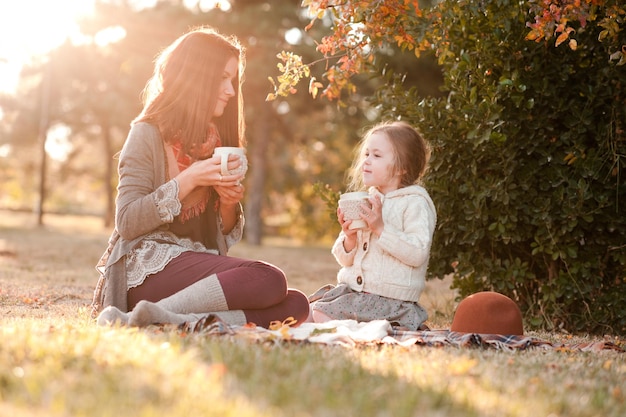 Mother drinking tea with kid daughter  sitting in sun light in park