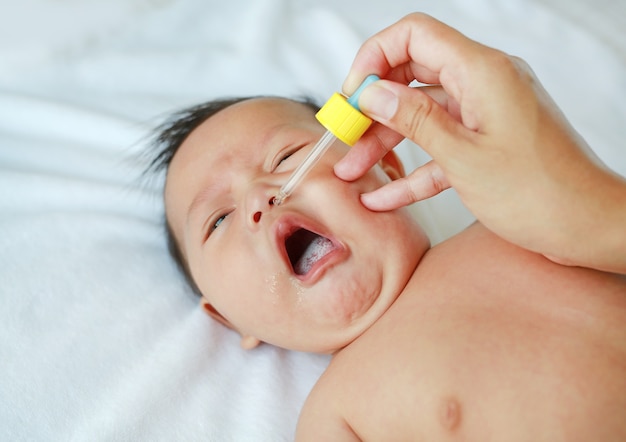 Mother dripping nasal drops for her infant. Baby healthcare concept.